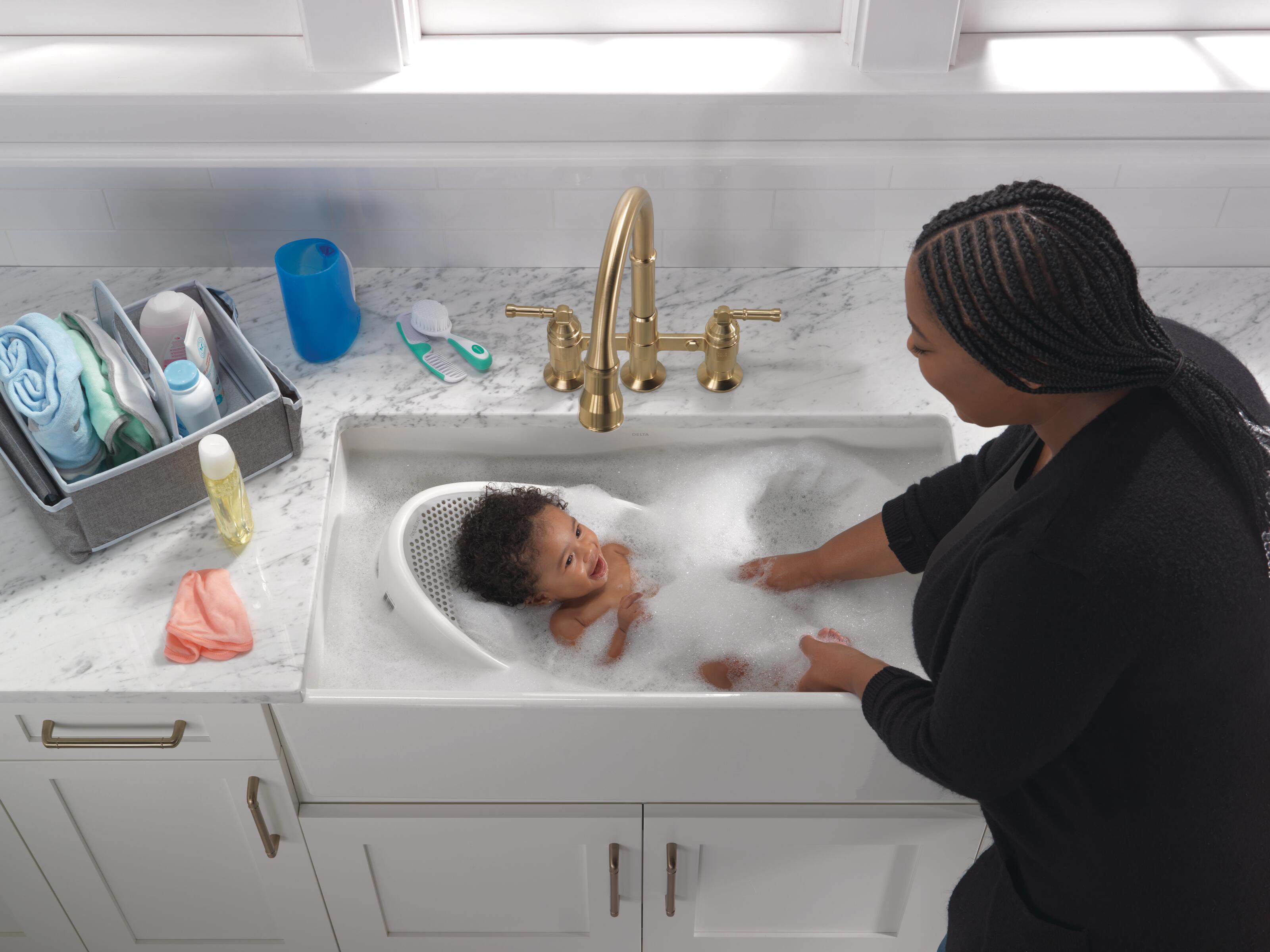 Woman bathing baby in kitchen sink with Delta faucet